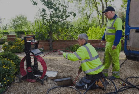 Wooley Water Sewer Trenchless staff check tools by an open manhole to make sure everything works safely before repair. A service van is close for easy access.