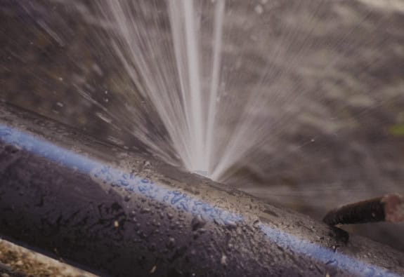 Water spraying from a cracked pipe shows the need for fast repair, which Wooley Water Sewer Trenchless can handle expertly.